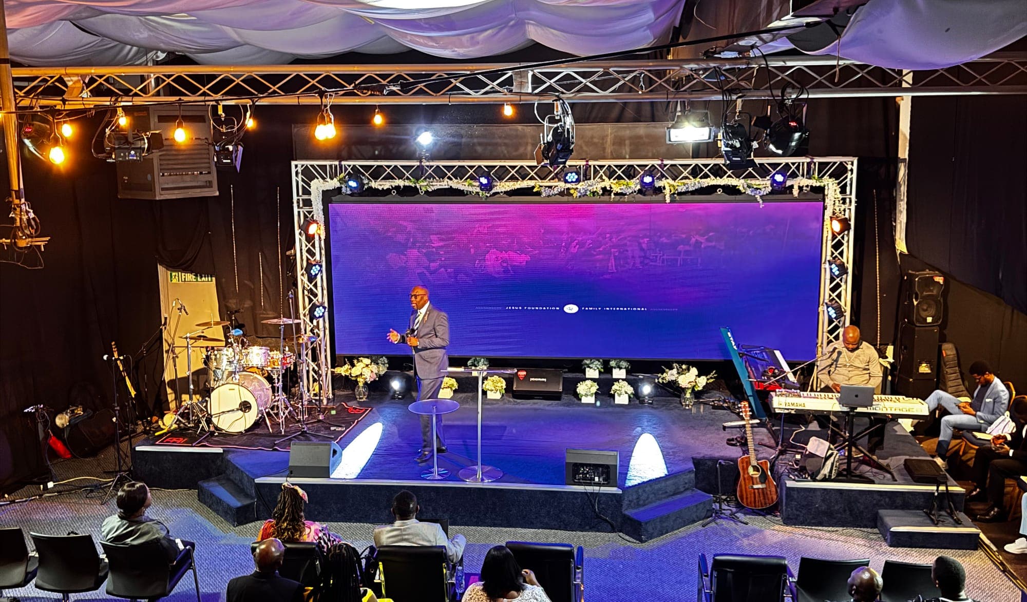 A preacher on stage in the church hall, with the band behind